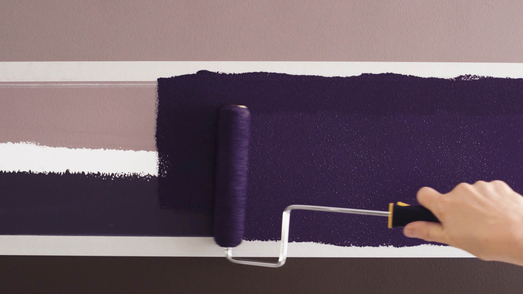 Rollen Sie die Farbe für die verwischte Linie auf die Wand auf Tragen Sie die Farbe zwischen den abgeklebten Linien mit einer kleinen Farbrolle auf
